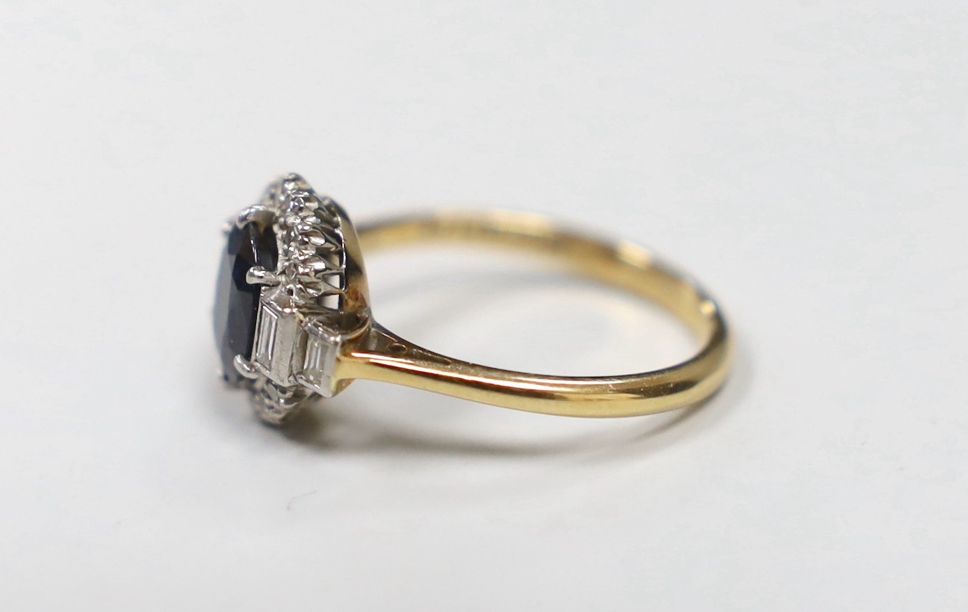 An Art Deco 18ct and plat, sapphire and diamond set oval dress ring with baguette cut diamond set shoulders, size P, gross weight 4.5 grams, in Art Deco celluloid box.